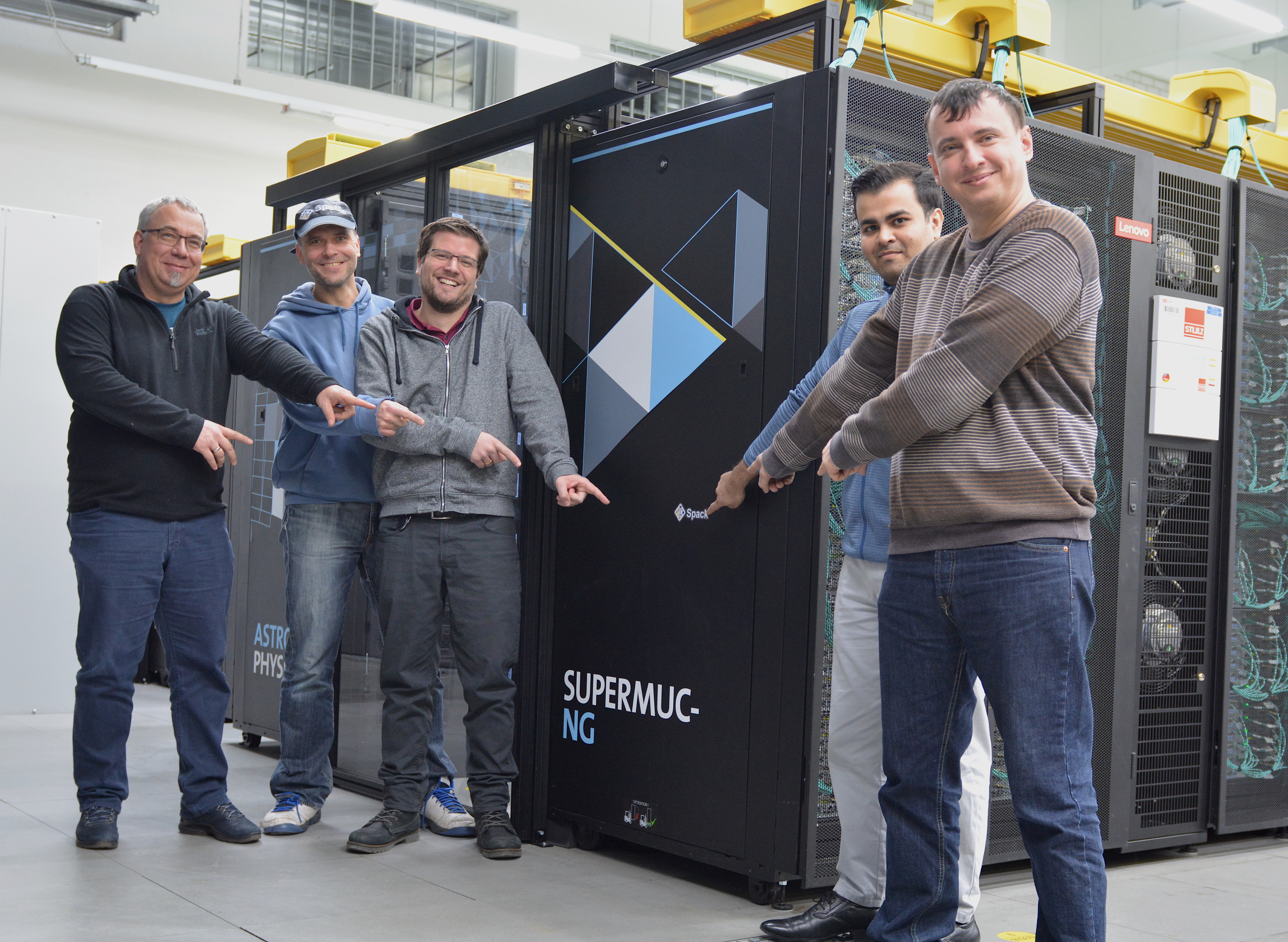 Members of the LRZ Spack team in front of SuperMUC-NG and pointing
at a Spack sticker placed on the rack front.